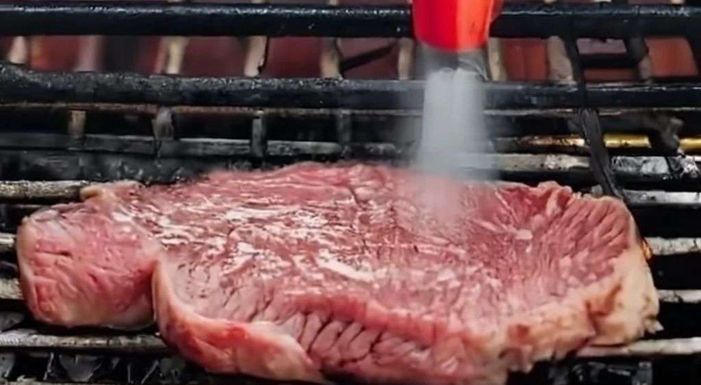 Spraying steak on the grill
